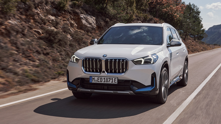 BMW iX1 U11 первого поколения, вид спереди в три четверти при движении по дороге BMW X Series BMW iX1 U11 первого поколения, вид спереди с поворотом в три четверти при движении по дороге