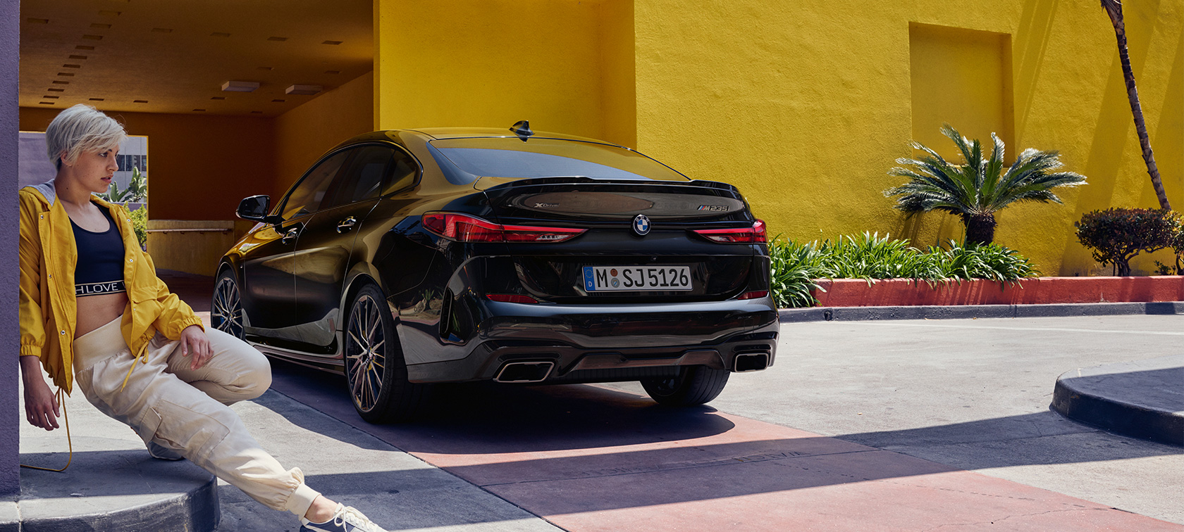 BMW M235i xDrive Gran Coupé Black Sapphire металлик F44 вид сзади с поворотом в три четверти с женщиной впереди