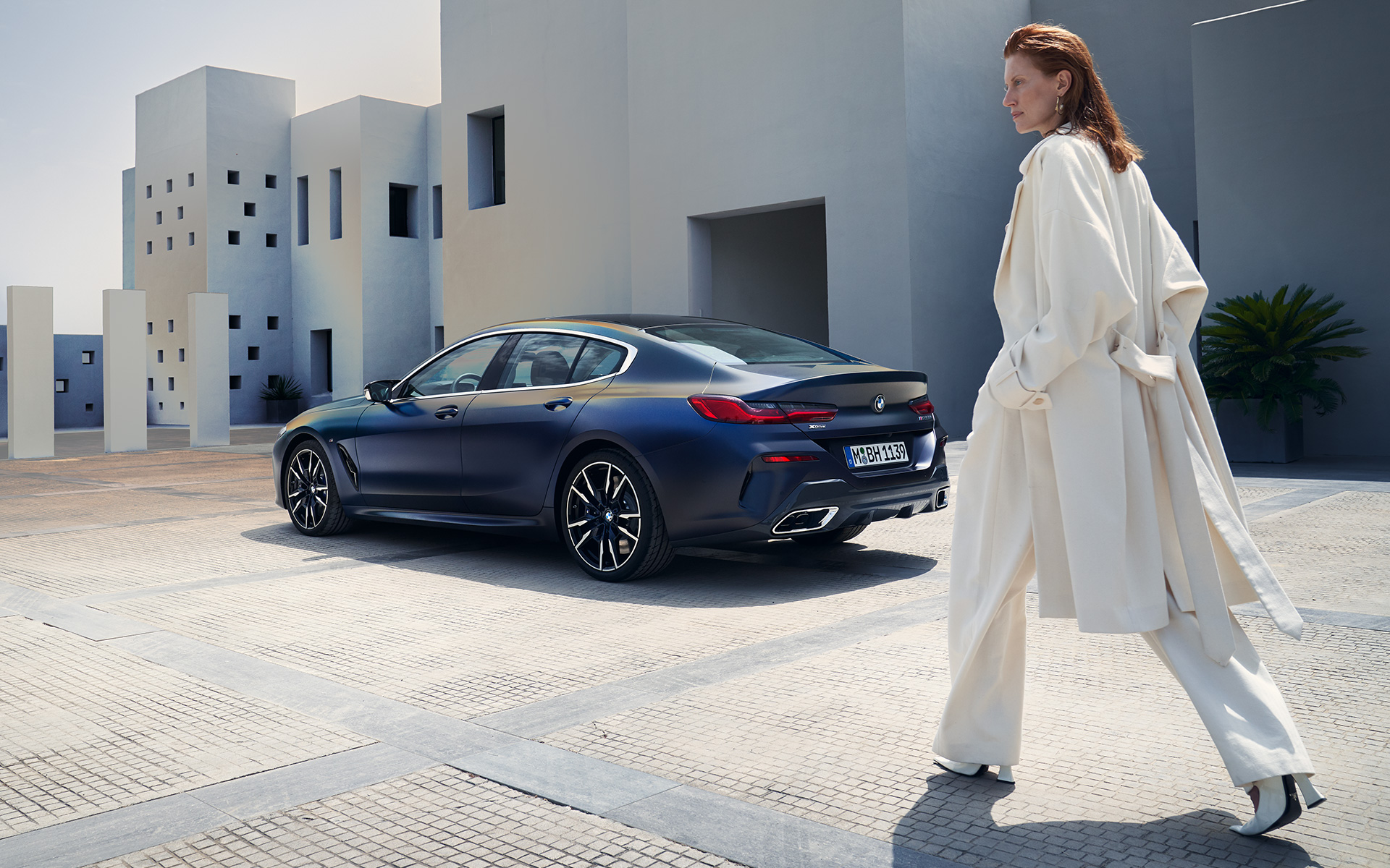 BMW M850i xDrive Gran Coupe G16 LCI Facelift 2022, вид сбоку с женщиной BMW M850i xDrive Gran Coupe G16 LCI Facelift 2022, BMW Individual Морозный Синий Танзанит металлик, вид сзади в три четверти с женщиной