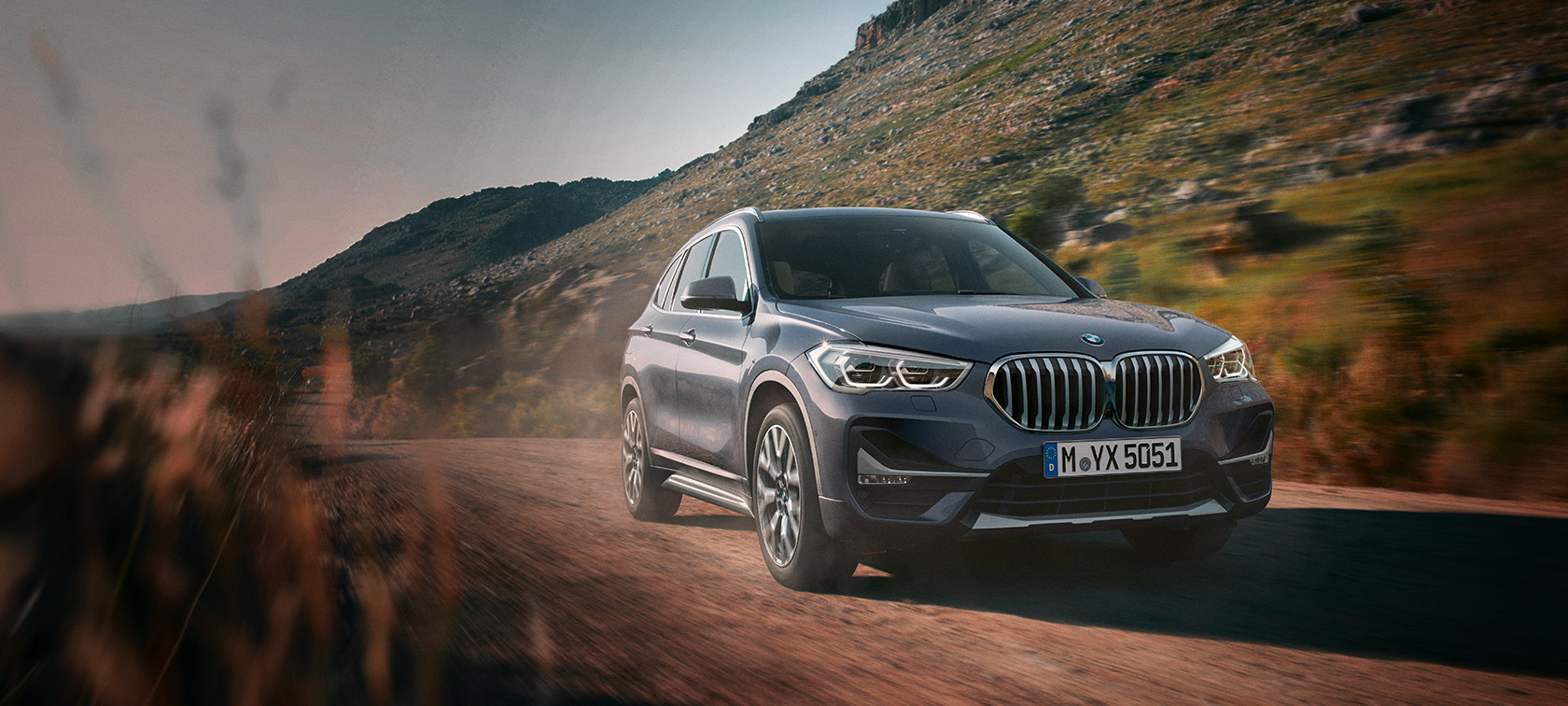 BMW X1 F48 LCI, Серый Шторм Бэй металлик, вид спереди в три четверти, в движении, перед горным пейзажем