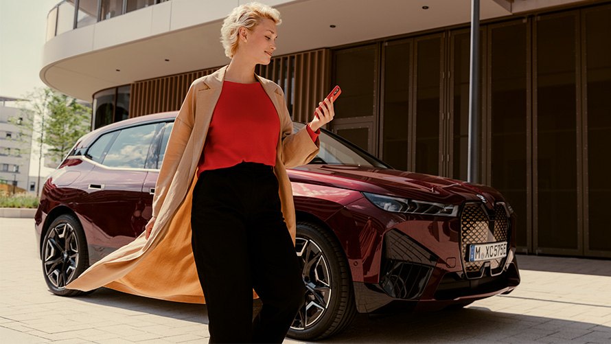 Приложение My BMW Женщина со смартфоном перед автомобилем BMW Женщина со смартфоном перед автомобилем BMW