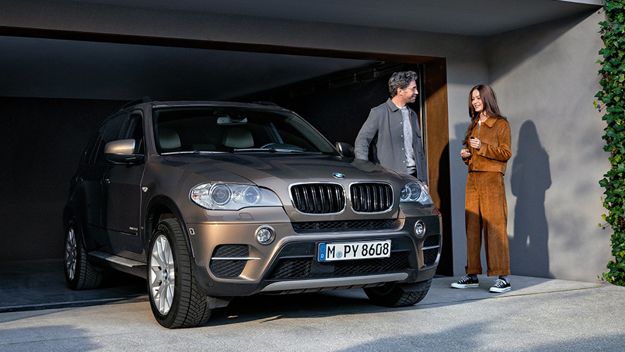 Автомобиль BMW и модели стоят перед гаражом BMW Value Service Автомобиль BMW и модели стоят перед гаражом